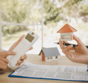 Photo of a someone holding a calculator and a miniature house