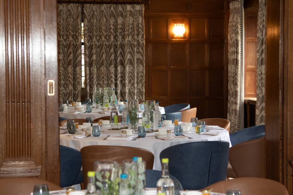 Round tables set for a Ladies First networking lunch with blue and brown chairs in a wood-paneled room.