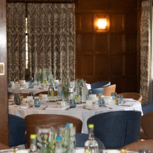 Round tables set for a Ladies First networking lunch with blue and brown chairs in a wood-paneled room.