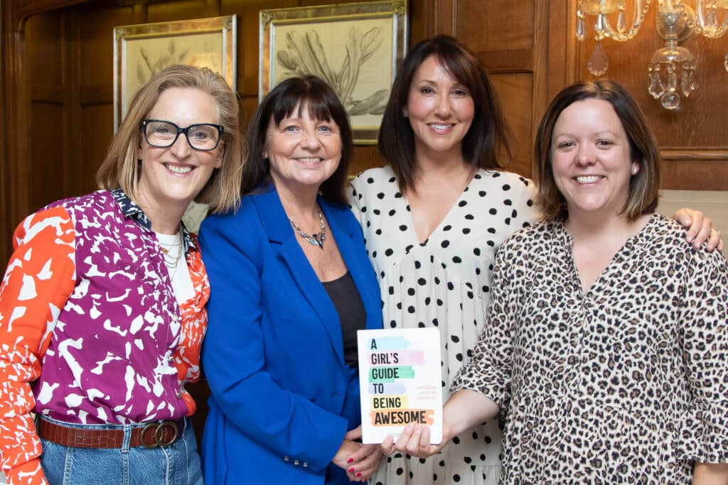 Four women at a networking event, one holding "A Girl's Guide to Being Awesome" book.