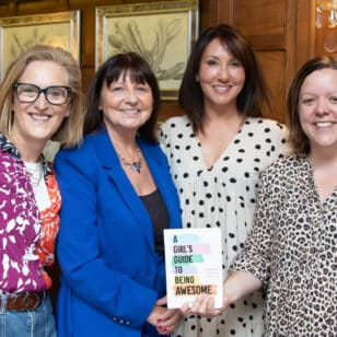 Four women at a networking event, one holding "A Girl's Guide to Being Awesome" book.