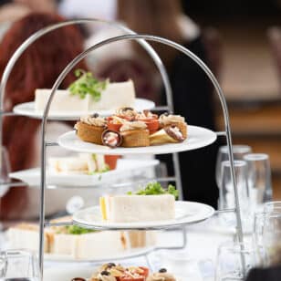Three-tier stand with gourmet sandwiches and pastries, glasses of water