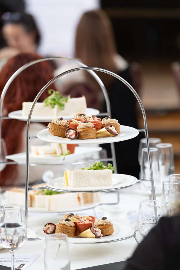 Three-tier stand with gourmet sandwiches and pastries, glasses of water