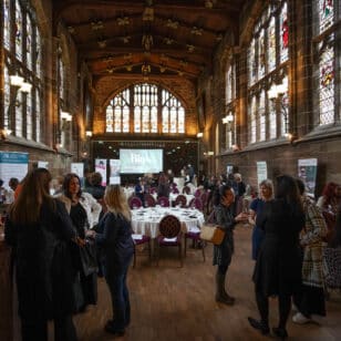 Networking event attendees converse in a hall with arched windows and a projector screen
