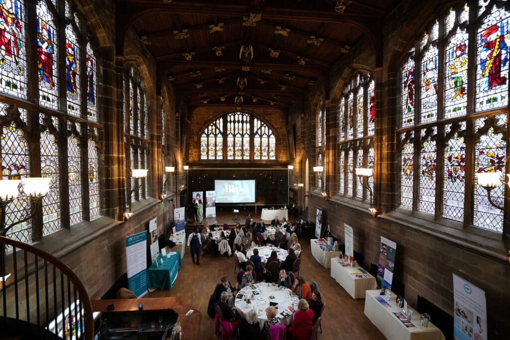 Conference attendees at Ladies First Networking event in a hall with stained glass windows