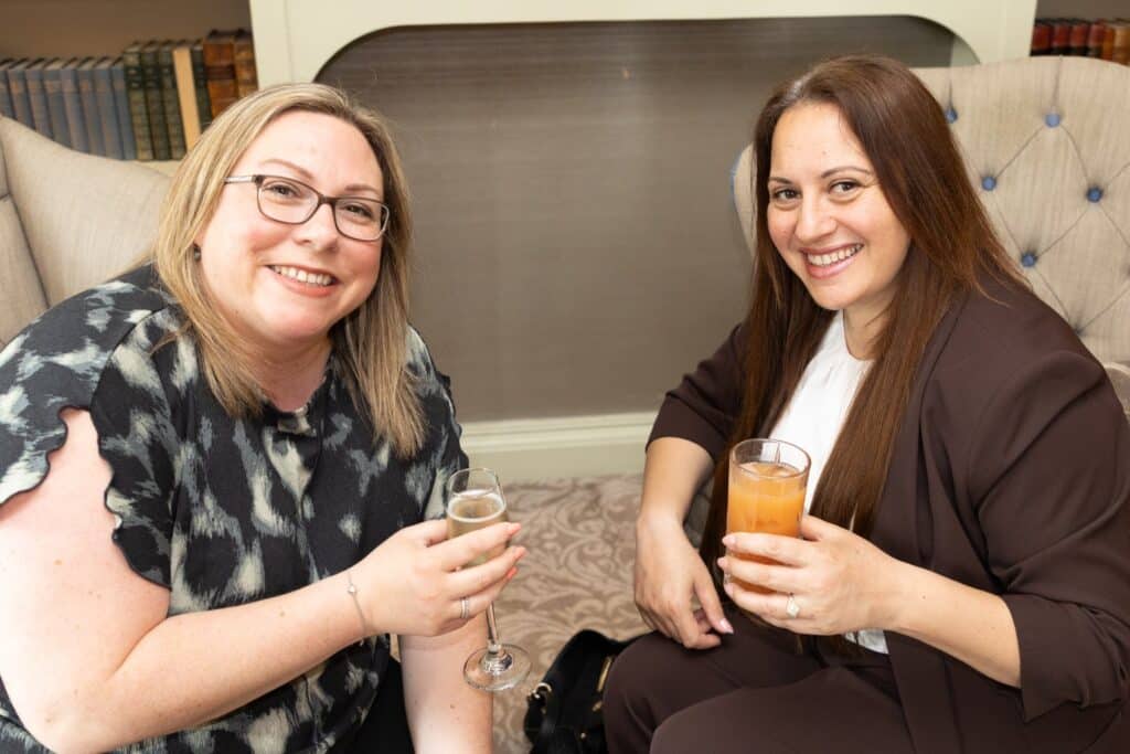 Two women smiling and holding drinks at the Ladies First Lunch event in June 2026.