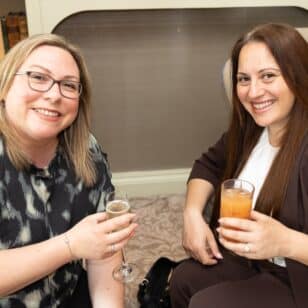 Two women smiling and holding drinks at the Ladies First Lunch event in June 2026.