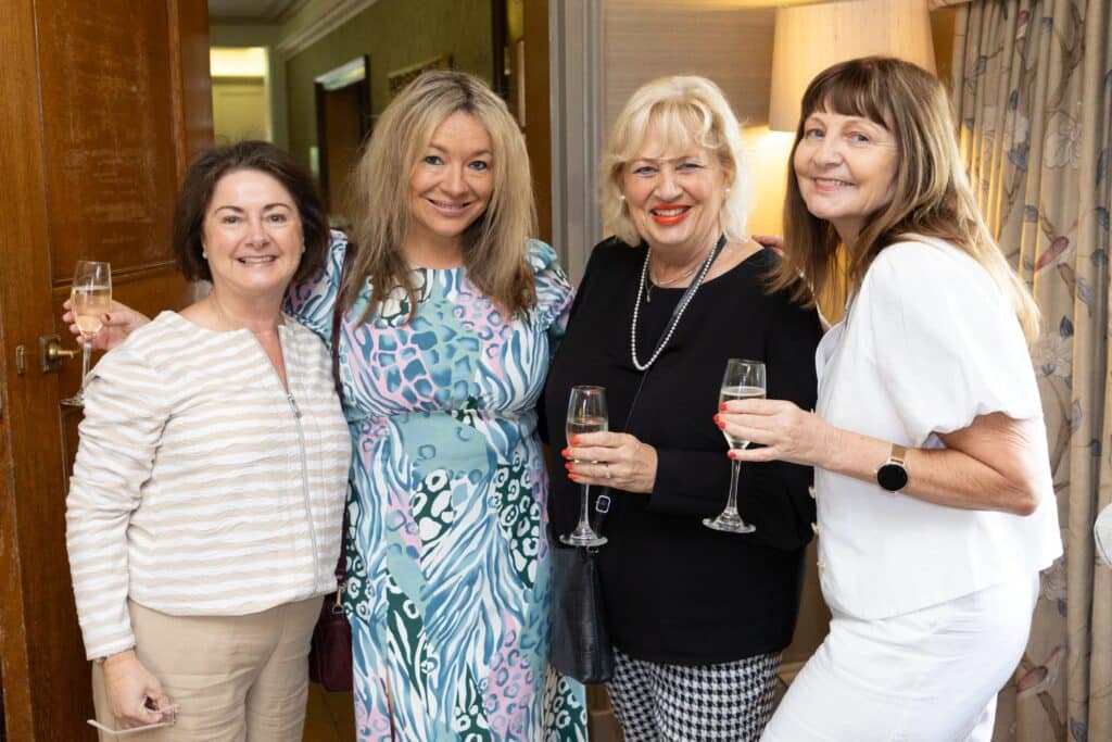 Four women smiling and holding champagne glasses at a Ladies First Lunch event.