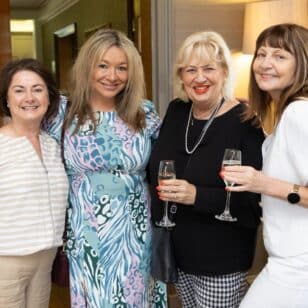Four women smiling and holding champagne glasses at a Ladies First Lunch event.