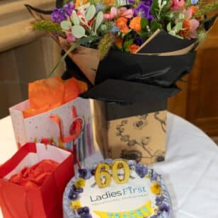 60th birthday cake with flowers and gifts at Ladies First professional development event.