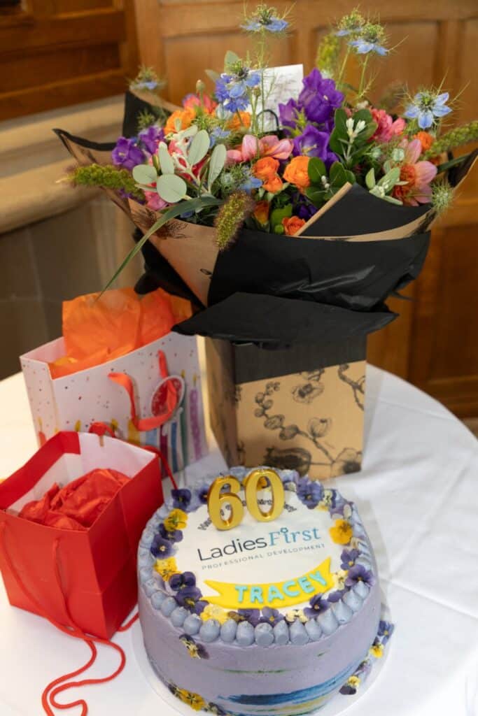 60th birthday cake with flowers and gifts at Ladies First professional development event.