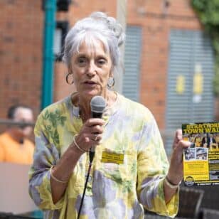 Woman with microphone and flyer for Stratford Town Walk, with text "Stratford Town Walk