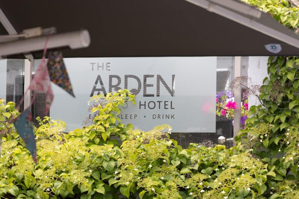 The Arden Hotel sign with lush greenery and colorful flowers