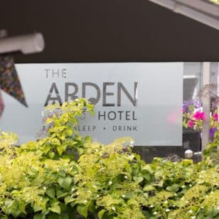The Arden Hotel sign with lush greenery and colorful flowers